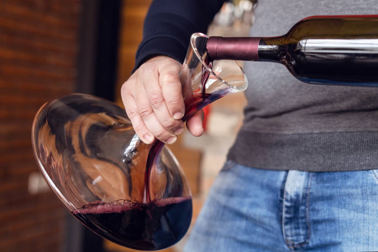 man decanting a bottle of red wine into a glass decanter